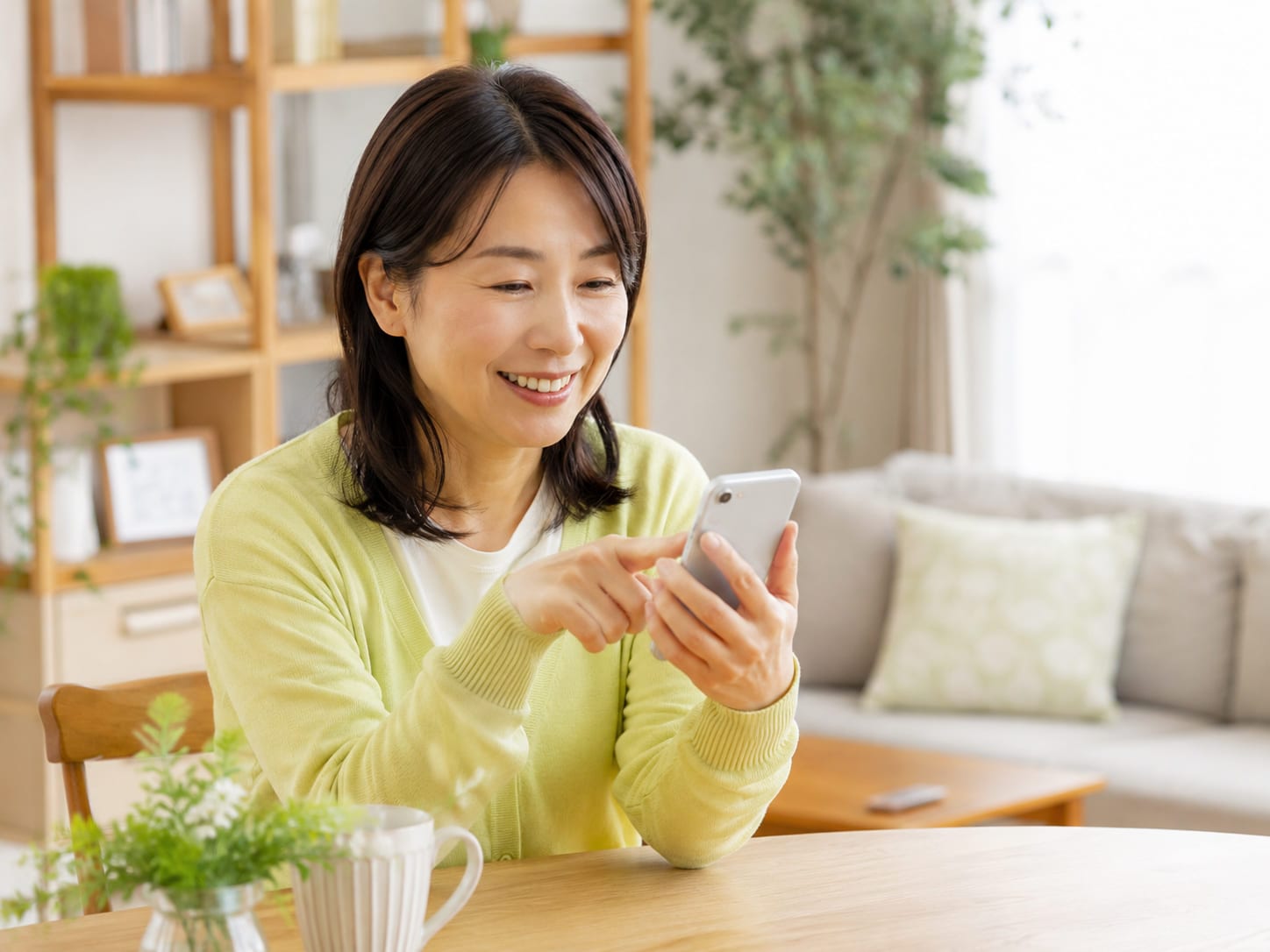 リビングのテーブルで、女性がスマートフォンを操作しながら微笑んでいる様子