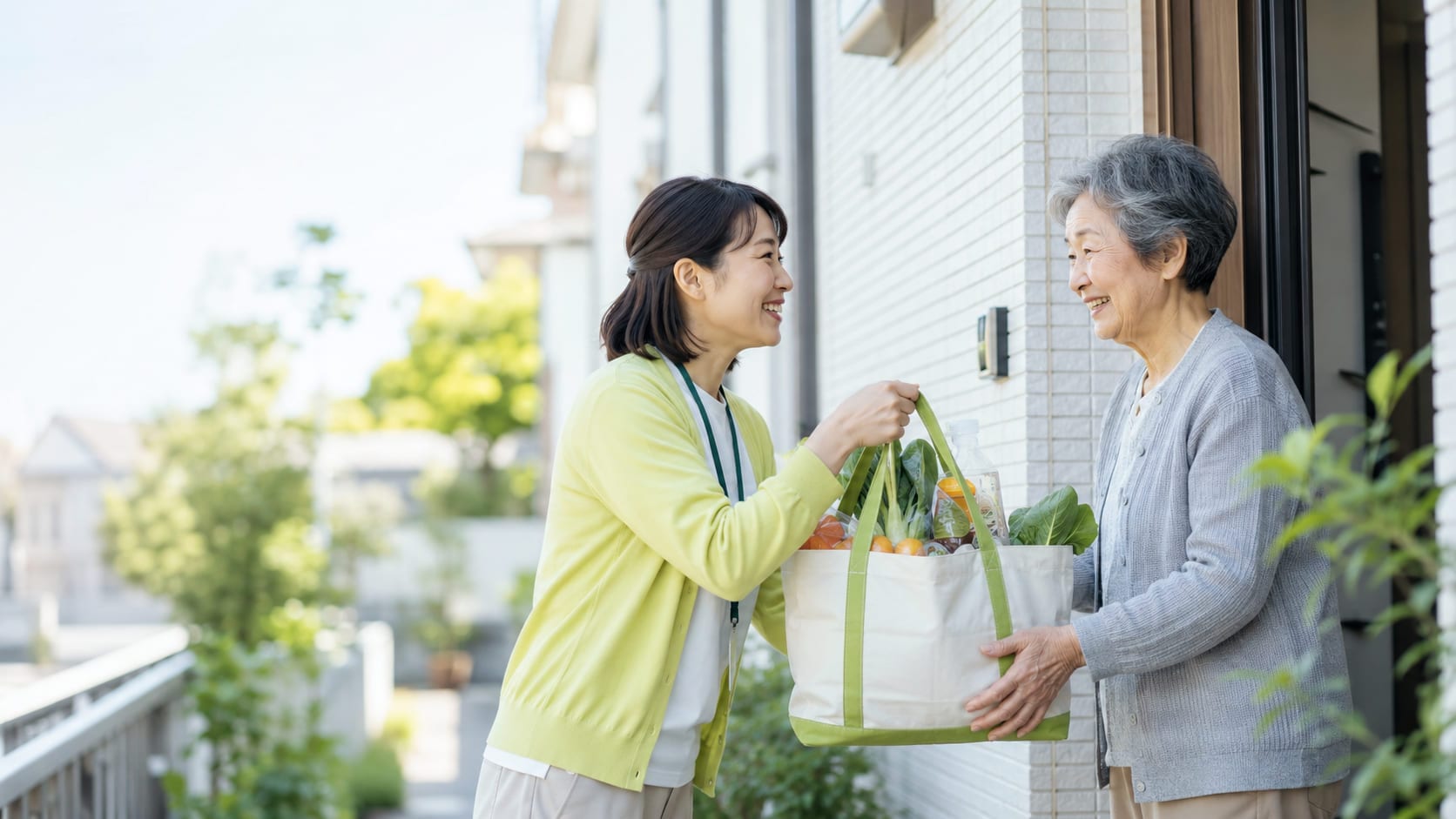 玄関先で、買い物代行のスタッフが野菜や飲み物の入ったトートバッグを高齢の女性に手渡している様子